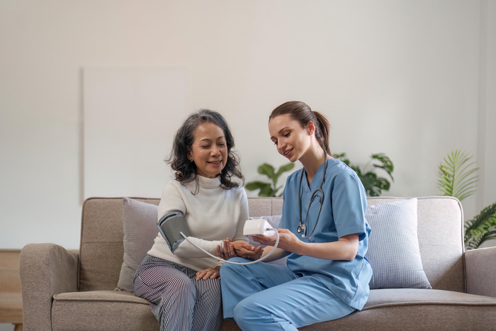 nurse doctor using digital tonometer check blood pressure for old asia female at home in elderly care cardiovascular medical visit, cholesterol problem. Home health care