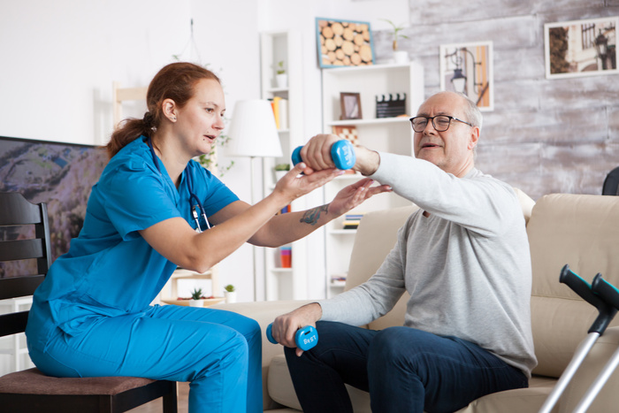 Senior man at home with home care nurse doing physical therapy