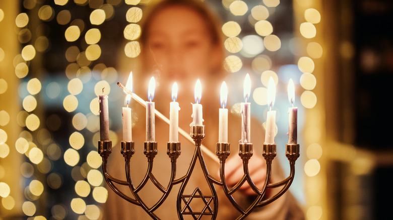 An elementary age child lighting the Menorah candles with a long match for Hanukkah celebration over the holiday.